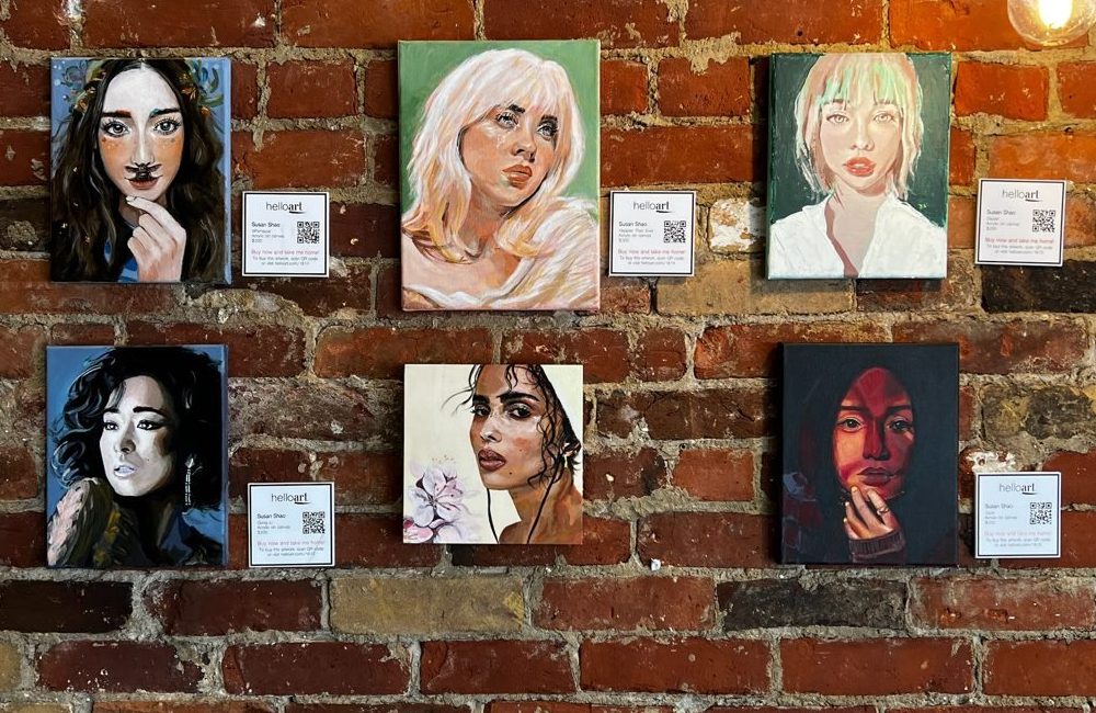 Six of Susan's portraits hanging on a brick wall at an art show